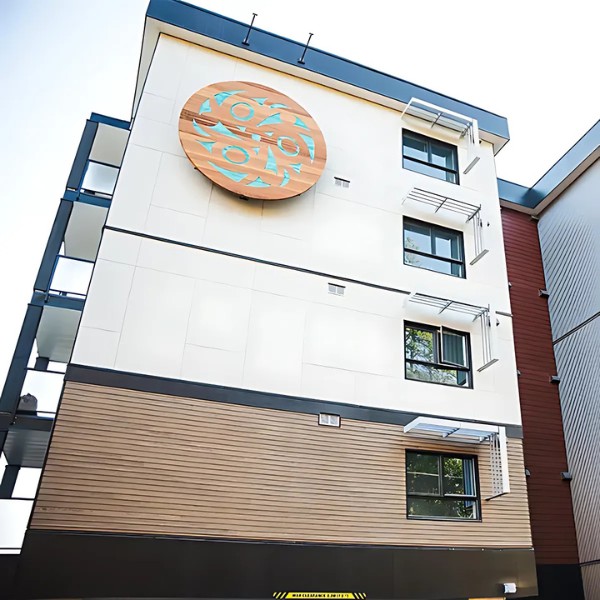 Modern multi-story building with white and brown paneling, featuring a large circular wooden decoration with blue patterns on the upper facade.