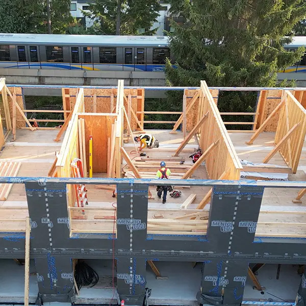 Workers building a wooden structure with a train passing in the background.