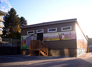 Wood stairs lead up to a building under a blue sky. The building has a painted mural with illustrated people waving hello