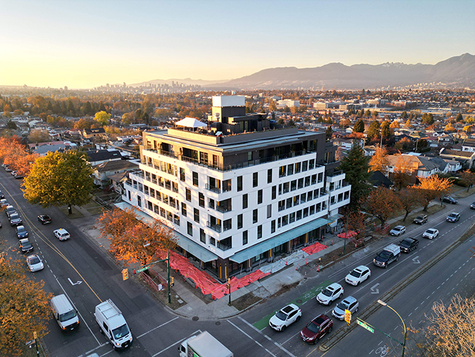 Six-storey white apartment building on a corner lot between two busy city streets