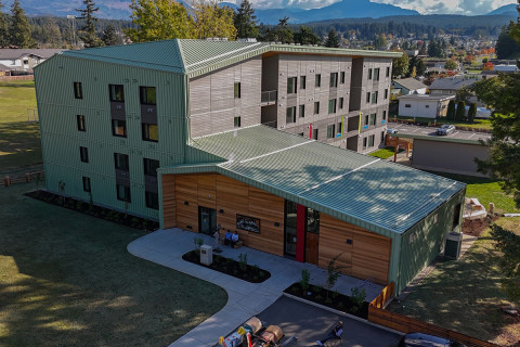 A modern urban complex with two glass high-rise buildings connected by a lower structure labelled "FOOD MARKET" and "OFFICES," located at a busy street intersection.