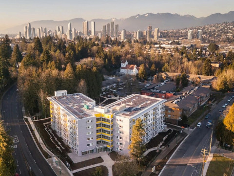 An aerial view of a residential area featuring a modern, multi-story apartment building with white and yellow accents.