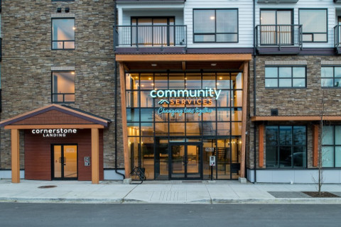 Front entrance of Cornerstone Landing, a brown stone apartment building with a "Community Services Changing Lives Together" sign.
