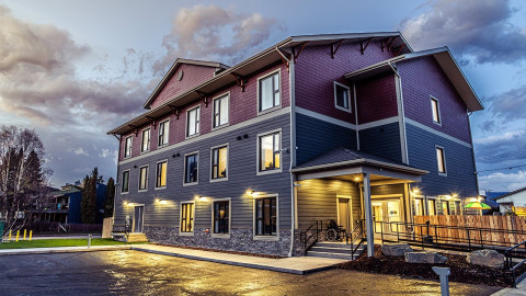 Three-storey purple and blue-sided building at dusk with exterior lights on.