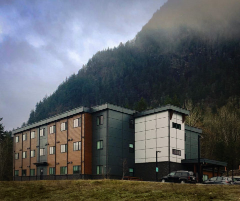 Three-storey apartment building with a tree-covered mountain in the background.