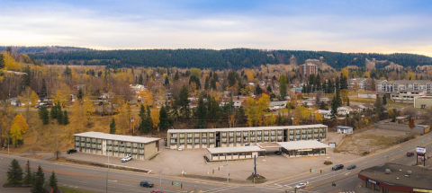 Aerial photo of a site with multiple long three-storey apartment buildings, backed by a large, tree-filled green space.