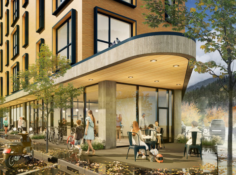 Urban street scene with a modern multi-story building featuring large windows and a concrete canopy, where people walk and sit at outdoor café tables; bicycles are parked nearby, autumn-colored trees line the street, and mountains rise in the background.