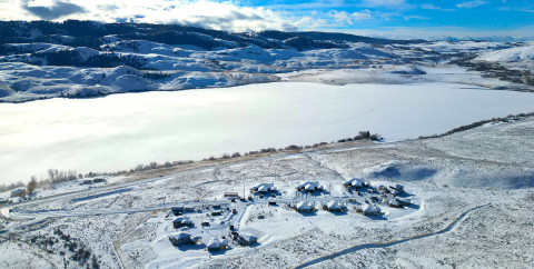 Aerial view of a snow-covered landscape with several houses situated beside a frozen lake.