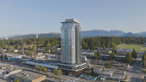 Aerial view of a 25-storey apartment tower standing tall above neighbouring stores and housing units.
