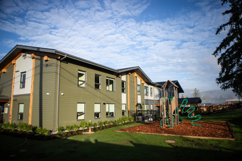 Two-storey building with deep green siding, with a children’s playground built beside it.