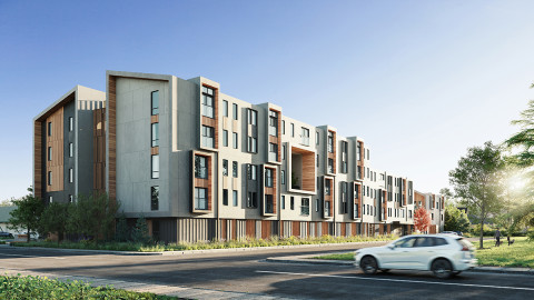 A modern four-story apartment building with a mix of concrete and wood accents, large windows, and geometric design elements, situated along a tree-lined street with a white car passing by under a clear blue sky.