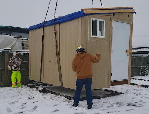 Two builders lowering a small wooden shelter to ground level.
