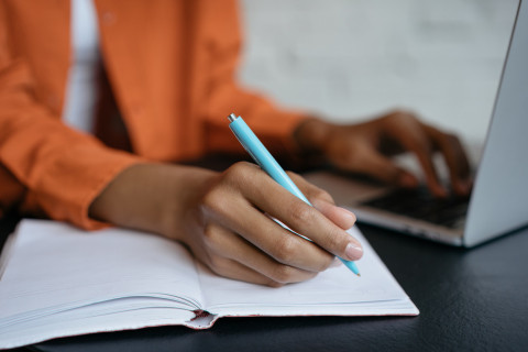Close-up of a student’s hand holding a pen and writing in a notebook while working at home.