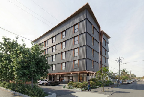 Modern five-story apartment building with corrugated metal facade, street-level shops, trees, parked cars, and pedestrians on a sunny street.
