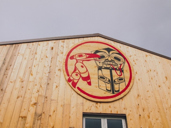 Front exterior of a large wooden building with Heiltsuk art featured on a raised wooden circle.