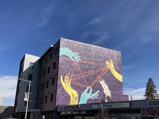 A multi-storey purple building with large painted blue and yellow hands holding string with a feather attached in the shape of a kite