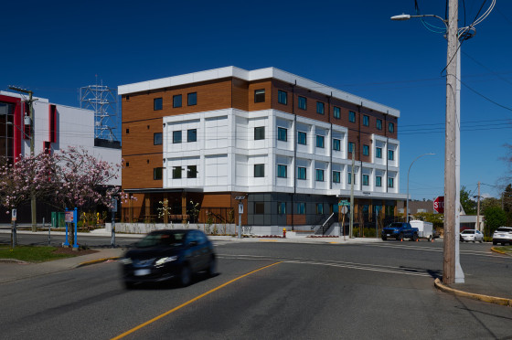 A four-storey white and brown building at an intersection, with cars driving by.