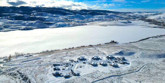 Aerial view of a snow-covered landscape with several houses situated beside a frozen lake.