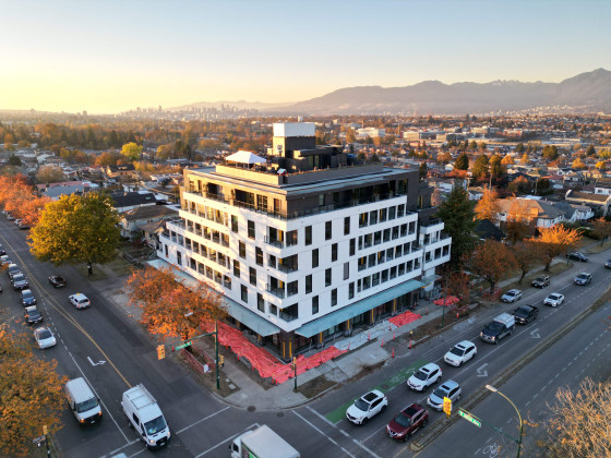 Six-storey white apartment building on a corner lot between two busy city streets.
