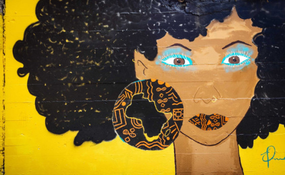 Mural of a black woman with short curly hair wearing black and orange circular earrings on yellow background