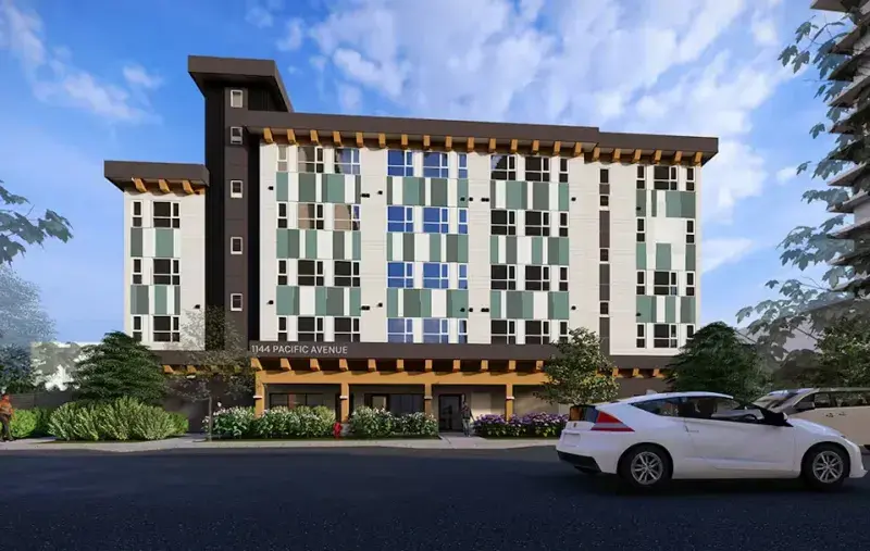 Architectural rendering of a mid-rise residential building with a patterned façade in green, blue, and white panels, ground-floor entrances, landscaped planting, and parked cars along a street under a blue sky